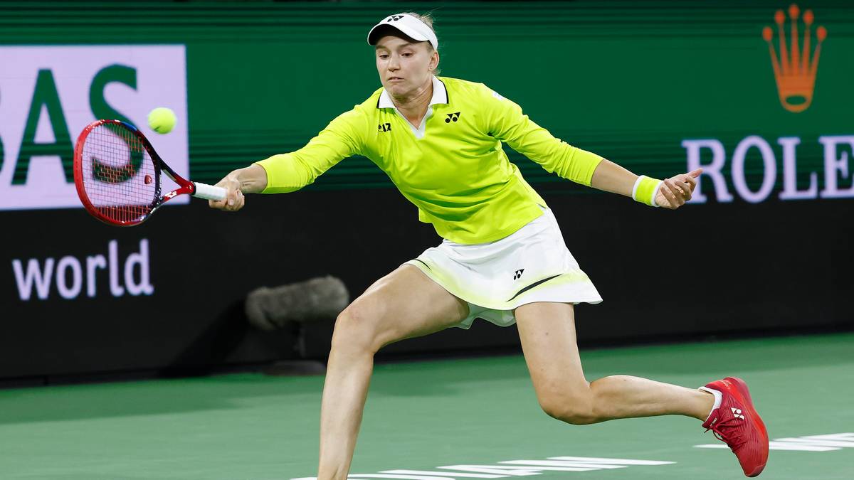 Tenisistka w ż&oacute;łtej bluzie i białej sp&oacute;dniczce wykonuje bekhendowy uderzenie.