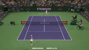 Kort tenisowy podczas meczu, widoczni zawodnicy, sędzia i widzowie na trybunach. Na bandach reklamowych logotypy sponsor&oacute;w.