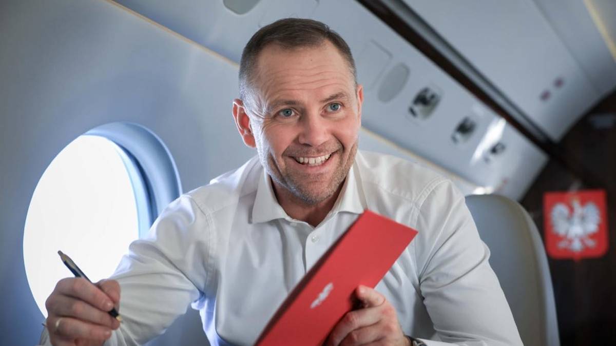 Mężczyzna w białej koszuli z dokumentem i długopisem w ręku, siedzący w samolocie.