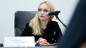 Kobieta siedząca przy stole z mikrofonem przed sobą, mówiąca.