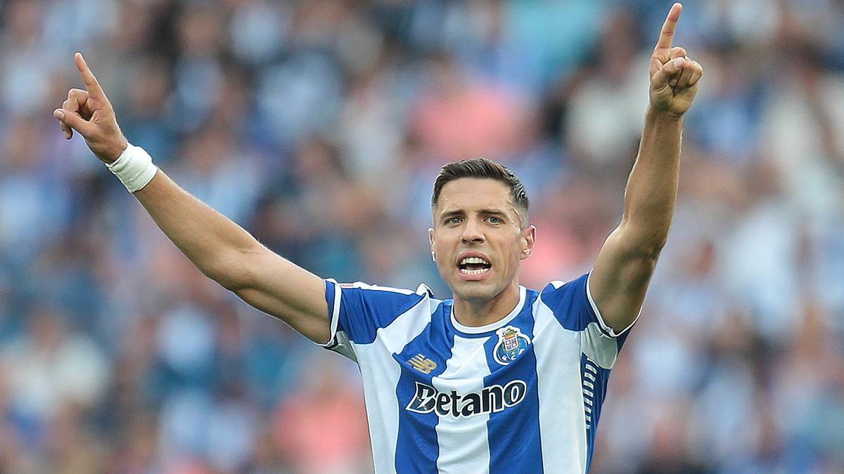 Piłkarz w niebiesko-białej koszulce FC Porto świętuje z podniesionymi rękami i palcami skierowanymi w g&oacute;rę.