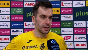 Marcin Komenda, zawodnik w żółtej koszulce sportowej, na tle sponsorów.