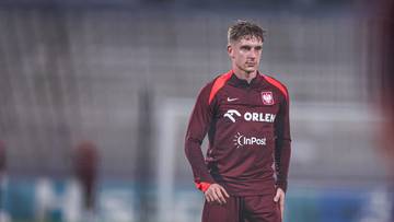 Młody piłkarz w bordowej koszulce reprezentacji Polski z logo Orlen i InPost stoi na boisku.