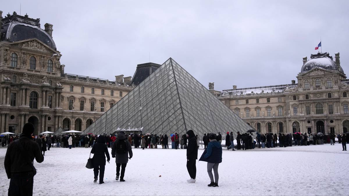 Szklana piramida Luwru z ludźmi na ośnieżonym placu.