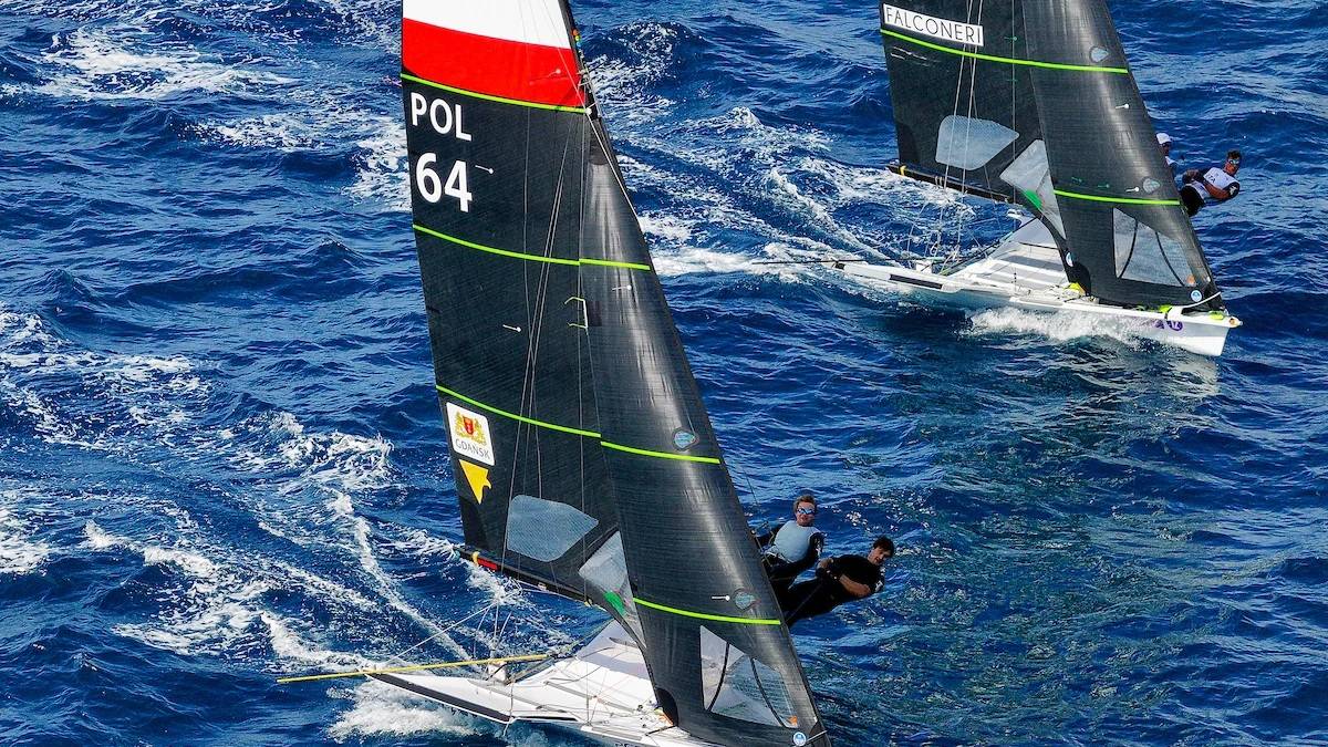 Dwie łodzie żaglowe klasy 49er rywalizujące na wodzie, z biało-czerwonym żaglem z napisem "POL 64" na jednej z nich.