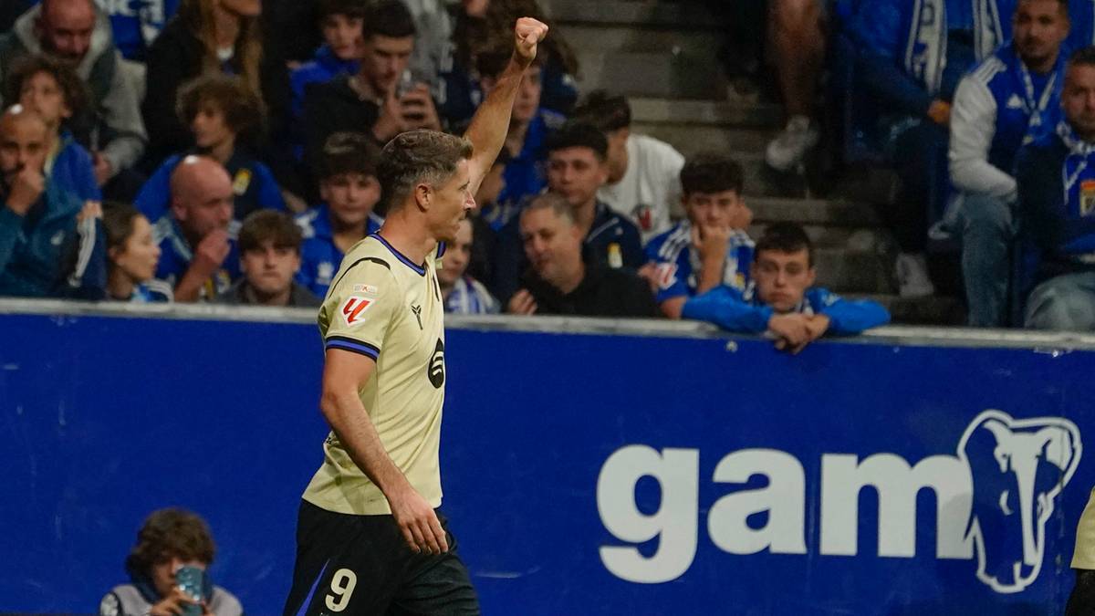 Piłkarz Robert Lewandowski w żółtej koszulce z numerem 9, unosząc prawą rękę do góry w geście radości po strzelonym golu, na tle trybun wypełnionych kibicami.