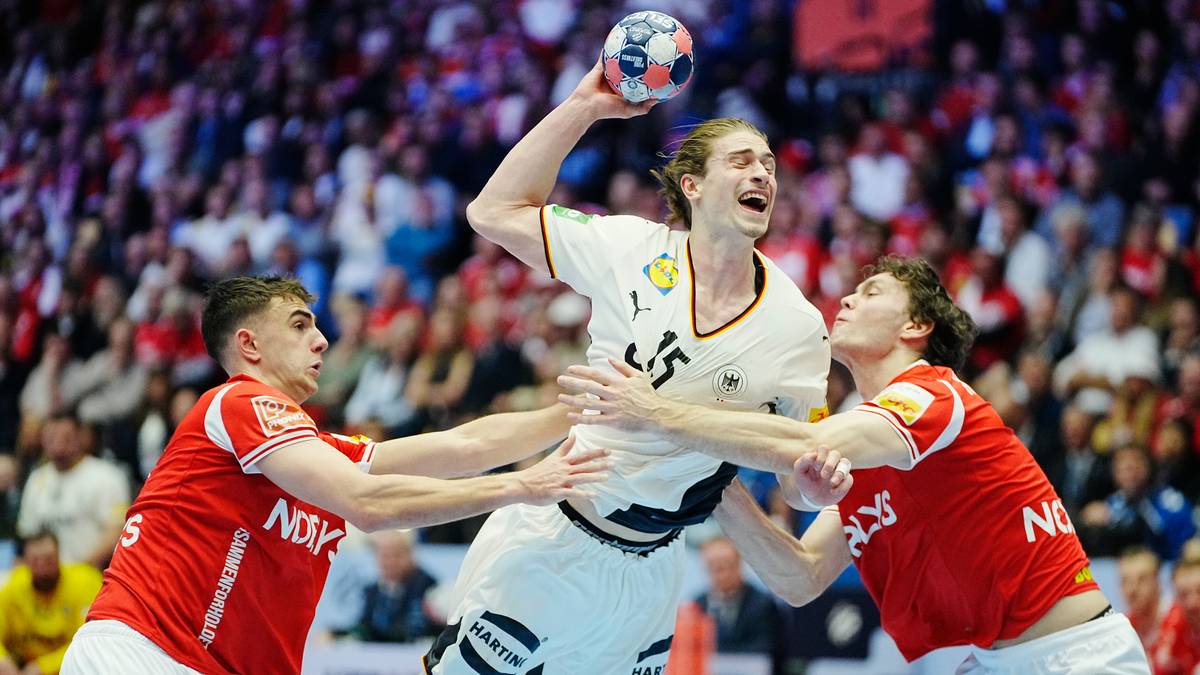 Piłkarz ręczny Danii w białej koszulce z numerem 15, podczas meczu, pr&oacute;buje rzucić piłkę do bramki, podczas gdy dwaj zawodnicy Niemiec w czerwonych koszulkach pr&oacute;bują go zatrzymać.