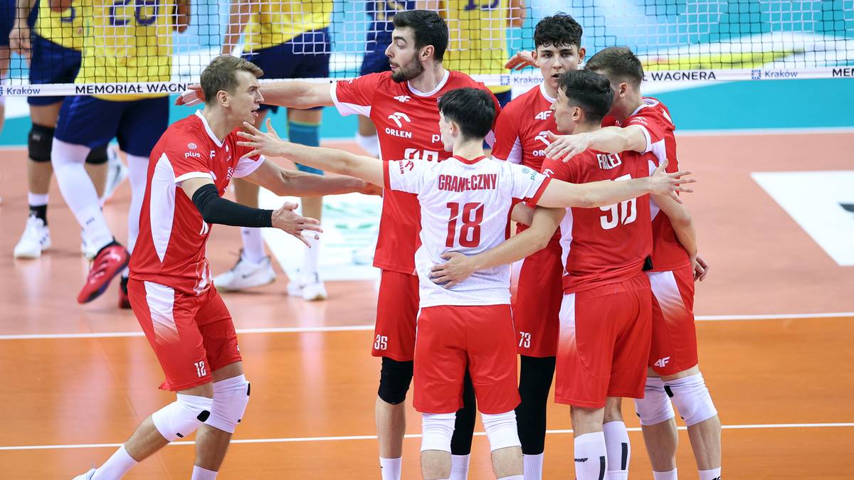 Drużyna siatkarzy w czerwonych strojach celebruje zwycięstwo, przytulając się i unosząc ramiona.