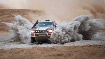 Samoch&oacute;d rajdowy Toyota z numerem zespołu Energylandia pokonuje pustynny odcinek specjalny, wzbijając tumany piasku.