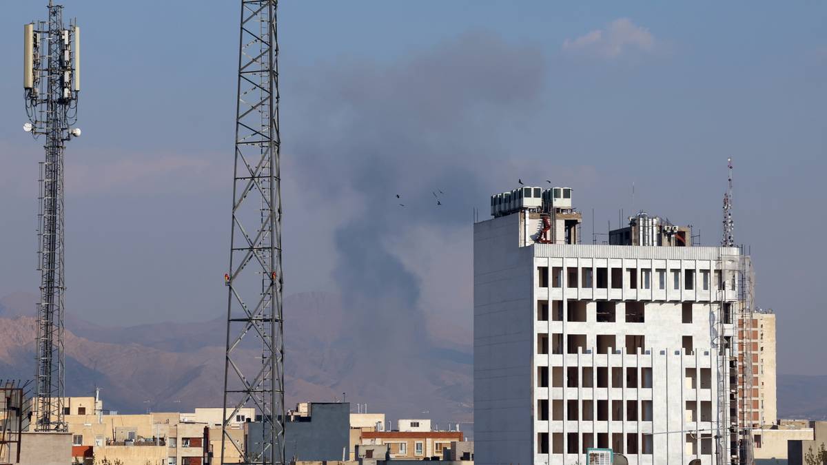 Widok na miasto z wieżami telekomunikacyjnymi i budynkami, w tle unoszący się dym.