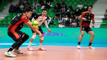 Trzech siatkarzy walczy o piłkę podczas meczu w hali sportowej.