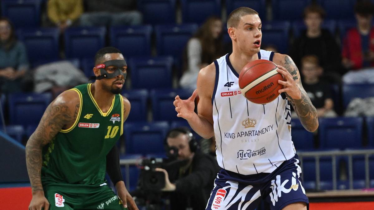 Dwóch koszykarzy na boisku, jeden z piłką w białej koszulce, drugi w zielonej koszulce z maską