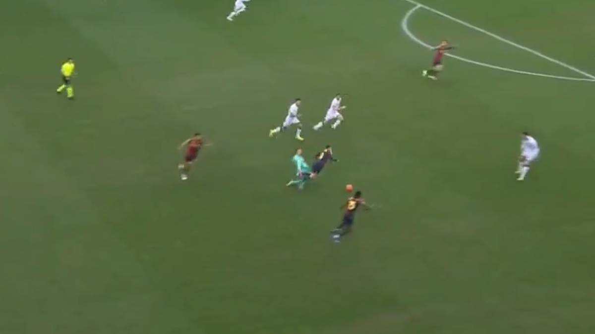 Piłkarze rywalizują o piłkę na boisku, w centrum znajduje się bramkarz w niebieskim stroju.