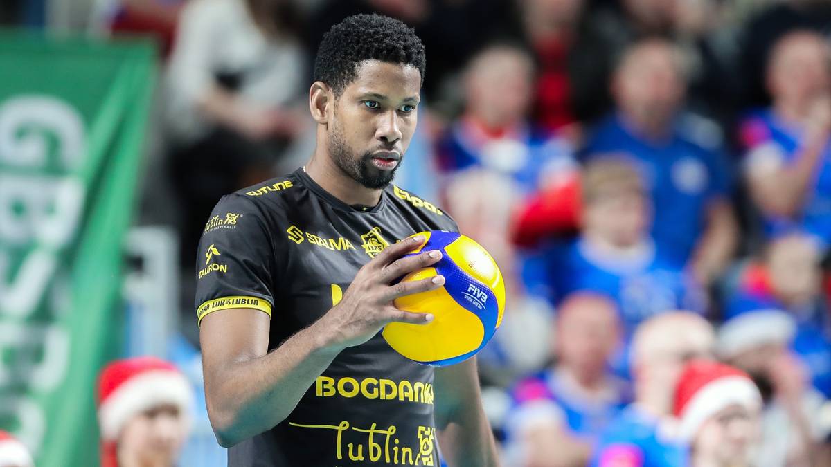 Siatkarz w czarno-żółtej koszulce trzyma piłkę do siatkówki w rękach.