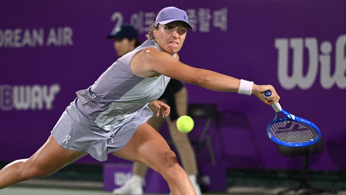 Iga Świątek podczas meczu tenisowego, uderzająca piłkę rakietą.