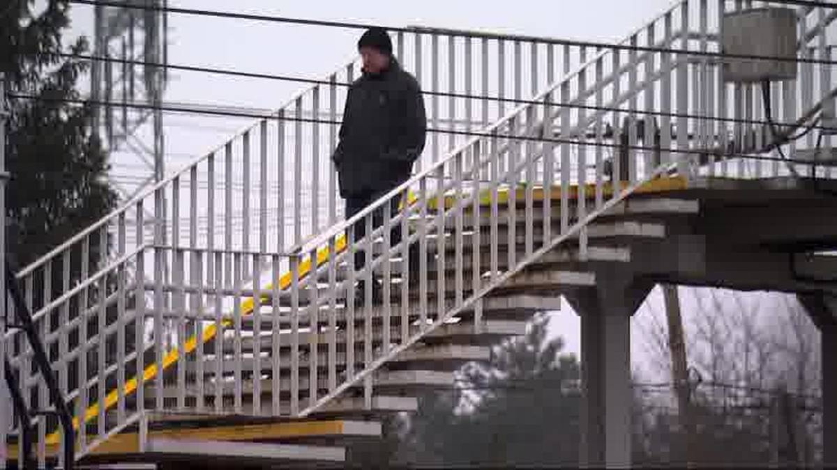 Mężczyzna w czapce i kurtce schodzi po białych metalowych schodach z ż&oacute;łtymi pasami ostrzegawczymi.