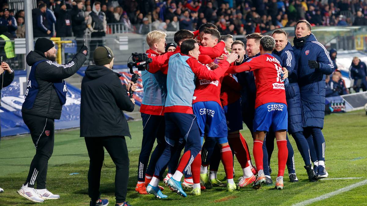 Grupa piłkarzy w czerwonych i niebieskich strojach świętuje zwycięstwo na boisku.