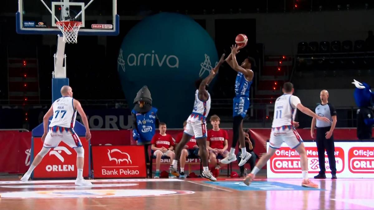 Dwóch koszykarzy walczy o piłkę podczas meczu, jeden w białym stroju z numerem 77, drugi w niebieskim stroju próbujący rzucić do kosza.