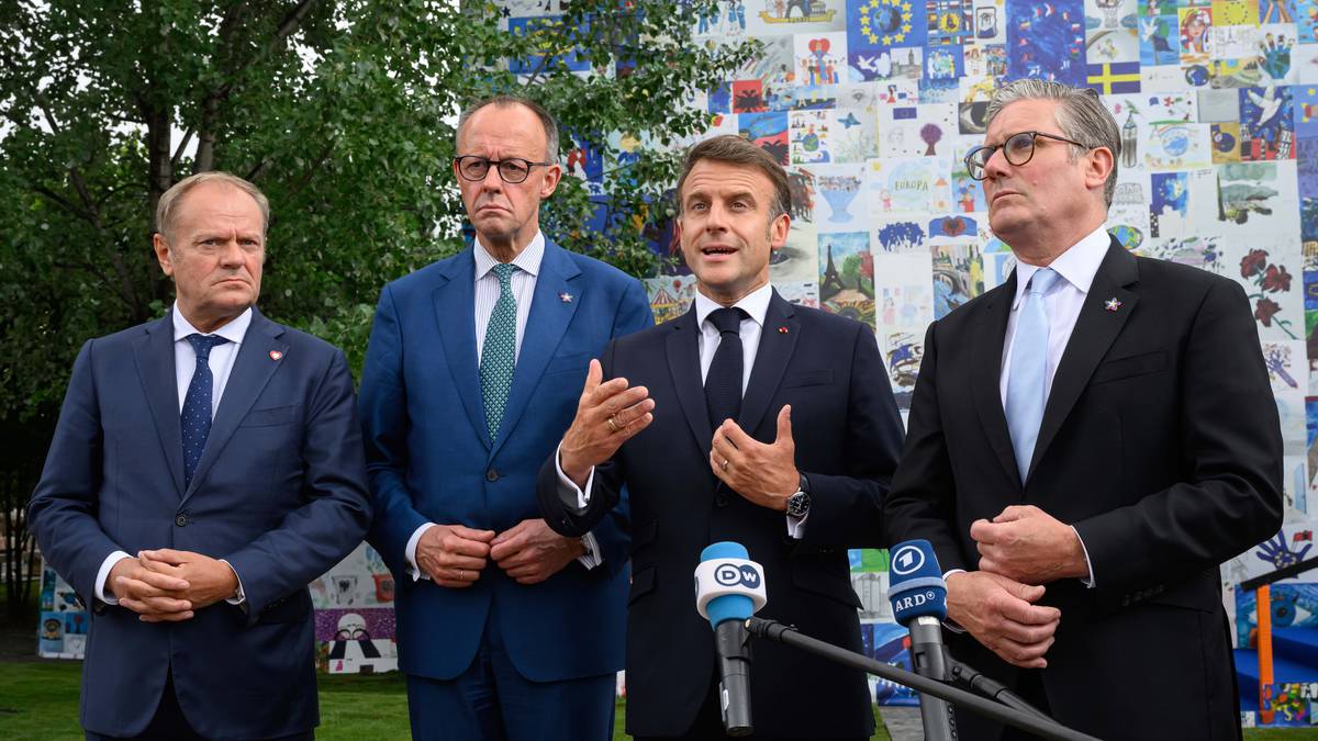 Czterech mężczyzn w garniturach stoi przed ścianą z grafikami, jeden z nich, Emmanuel Macron, przemawia do mikrofon&oacute;w.