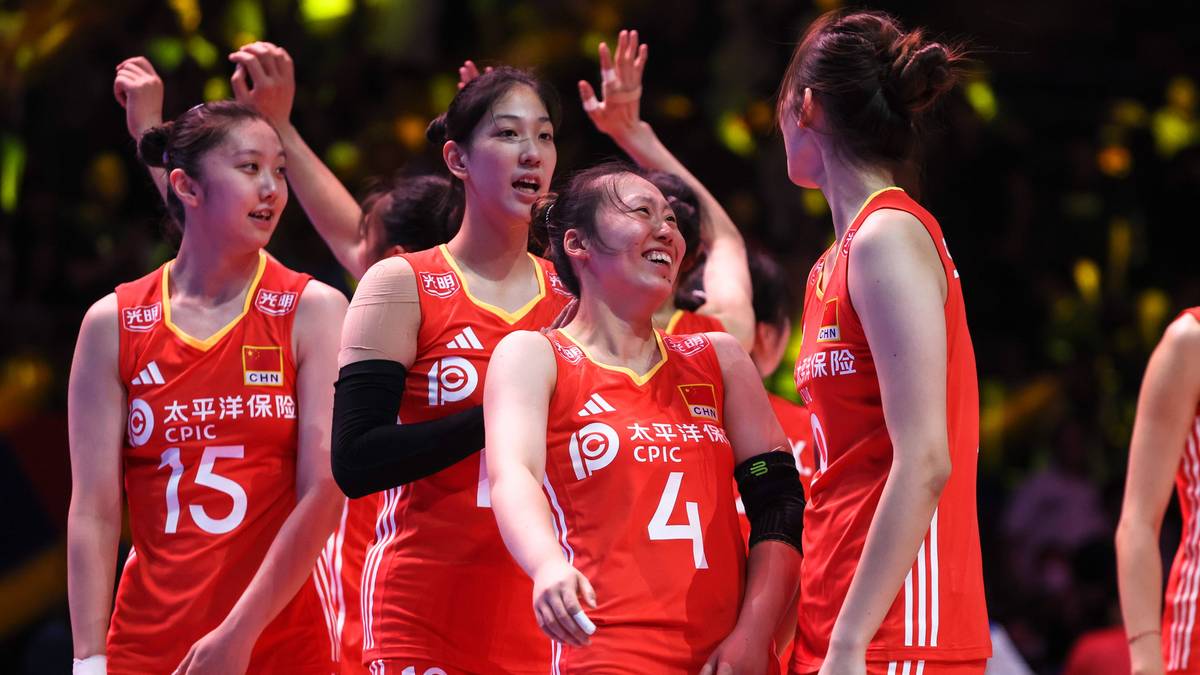 Drużyna siatkarek w czerwonych strojach z białymi napisami i numerami na plecach, świętująca na boisku.