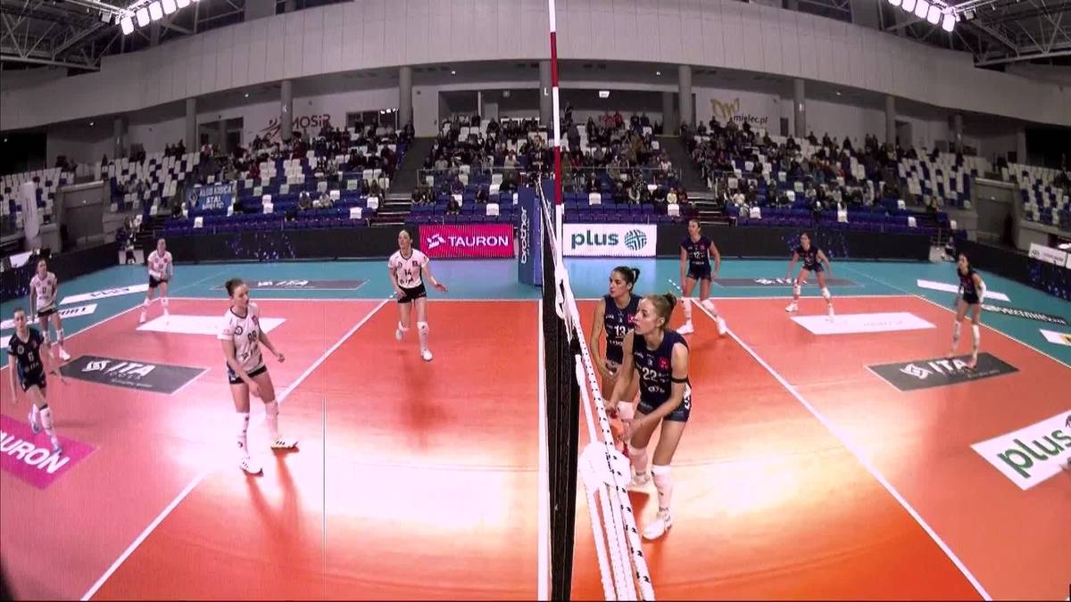 Dwie drużyny siatkarskie grające na boisku, jedna w czarnych strojach, druga w białych.