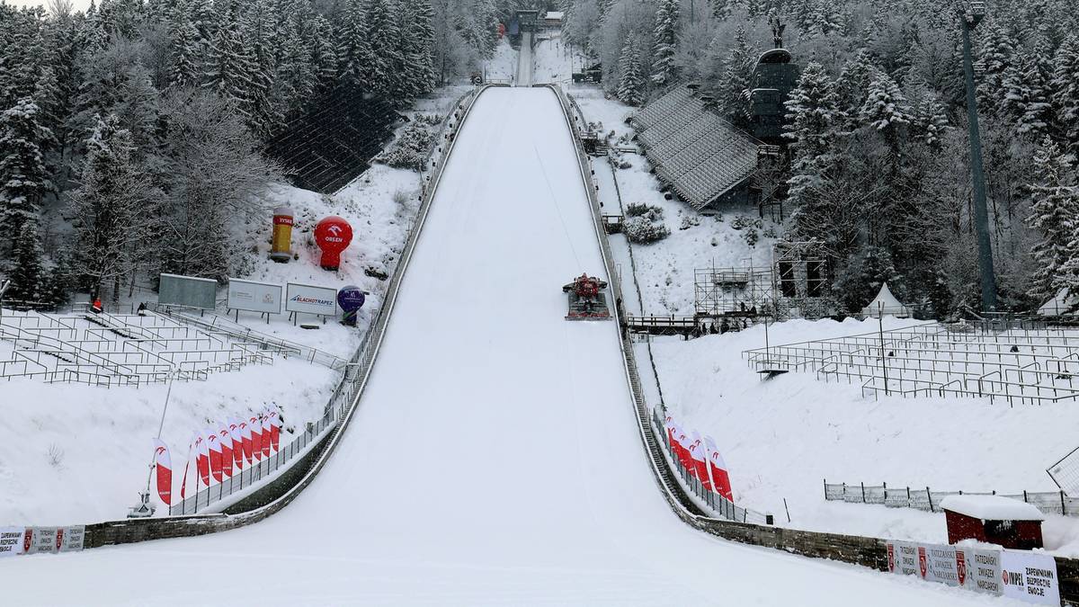 Zimowa skocznia narciarska otoczona zaśnieżonym lasem.
