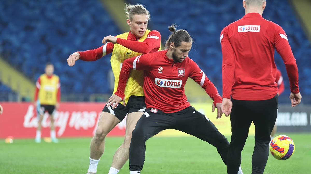 Piłkarze w czerwonych strojach rywalizują o piłkę na boisku.