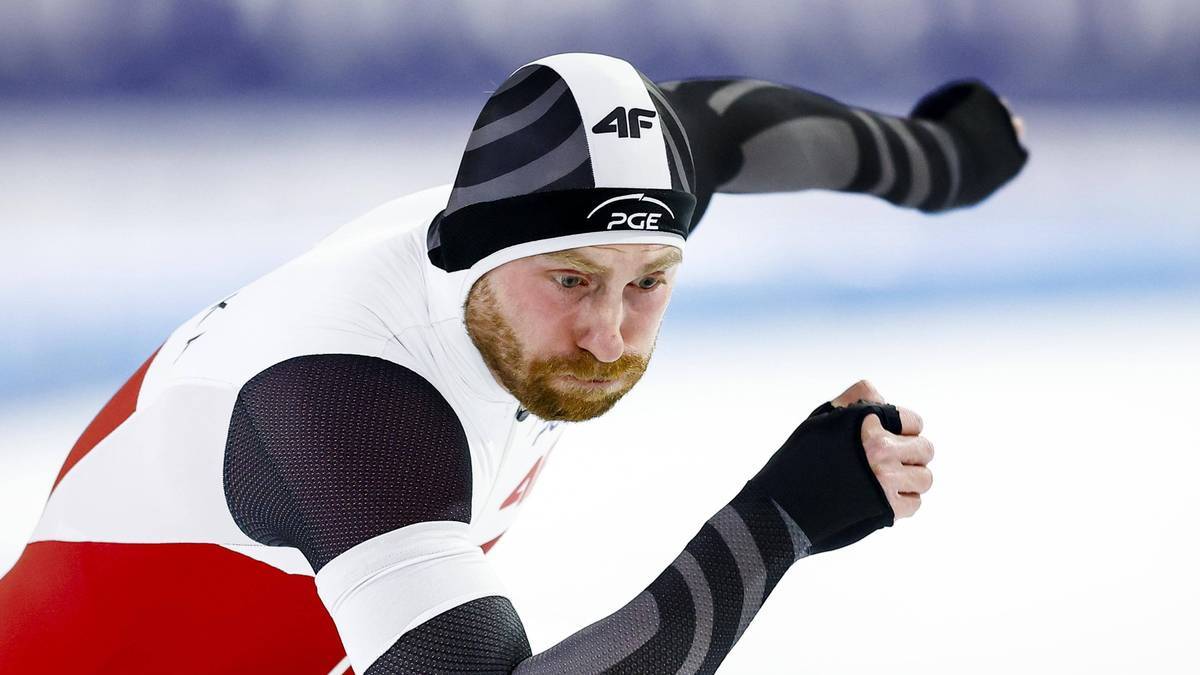 Łyżwiarz szybki w białym stroju z czerwonymi elementami i czarno-białą czapką