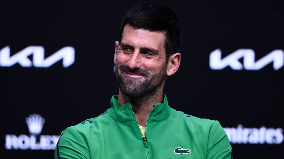 Novak Djoković w zielonej kurtce, uśmiechnięty.