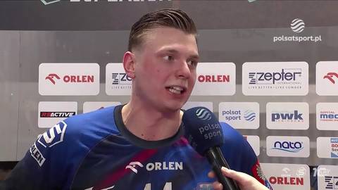 Młody mężczyzna z kr&oacute;tkimi, zaczesanymi włosami, ubrany w niebiesko-czarną koszulkę sportową z logotypem "ORLEN" i "44", odpowiada na pytanie dziennikarza przed mikrofonem z logo "Polsat Sport". W tle znajduje się tablica z wieloma logotypami sponsor&oacute;w.