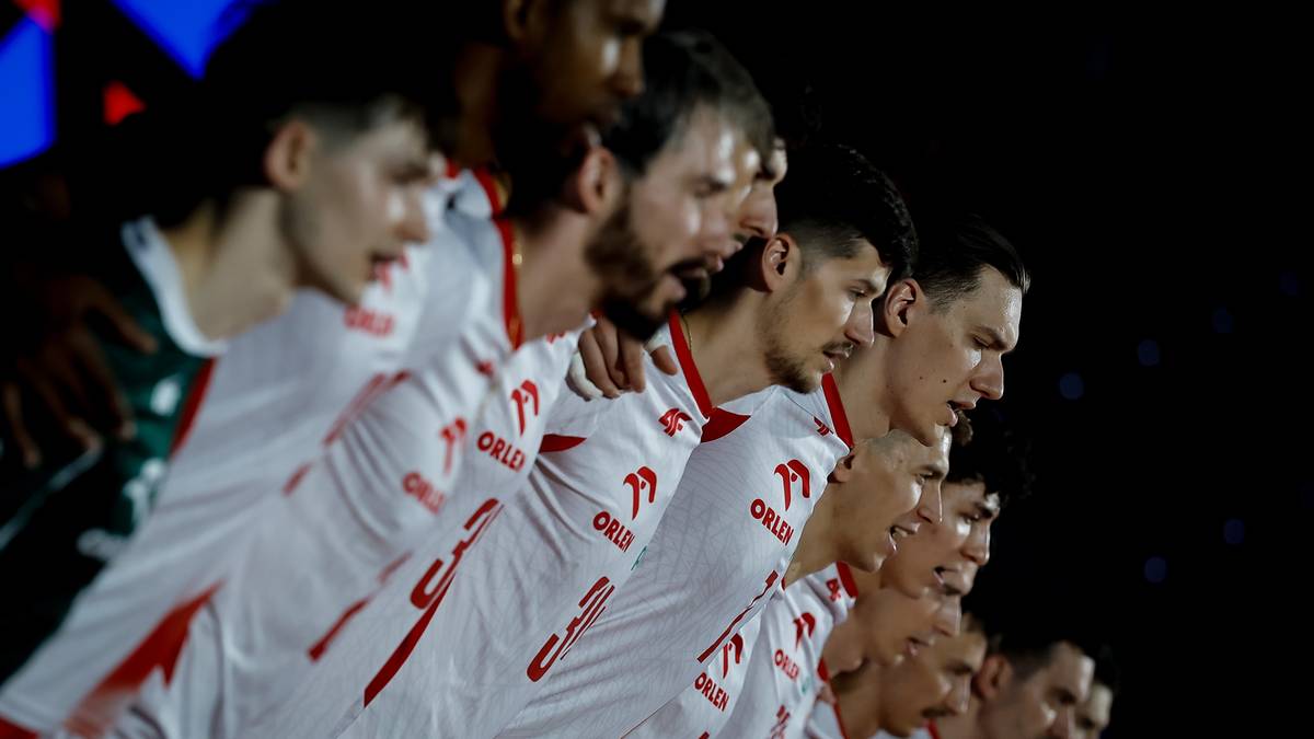 Grupa sportowców w białych koszulkach z czerwonymi akcentami, patrzą w jednym kierunku z wyrazem skupienia na twarzach.