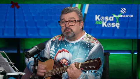 Roman Kosecki gra na gitarze w świątecznym swetrze.