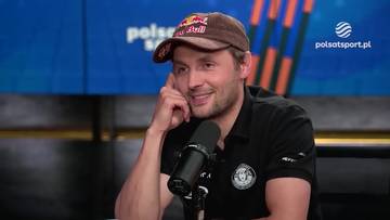 Mężczyzna w czapce z daszkiem z logo Red Bull i czarnym t-shircie siedzi przy mikrofonie i uśmiecha się, podczas wywiadu.