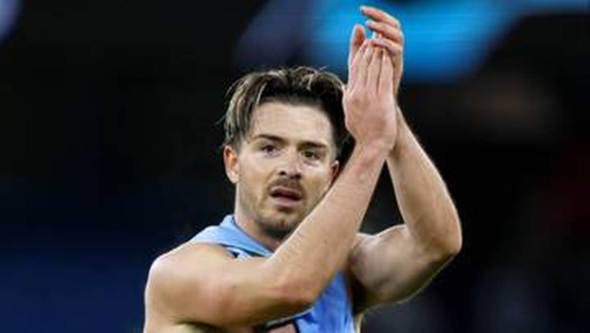 Piłkarz Manchesteru City, Jack Grealish, z uniesionymi i klaszczącymi dłońmi, z lekkim uśmiechem na twarzy.