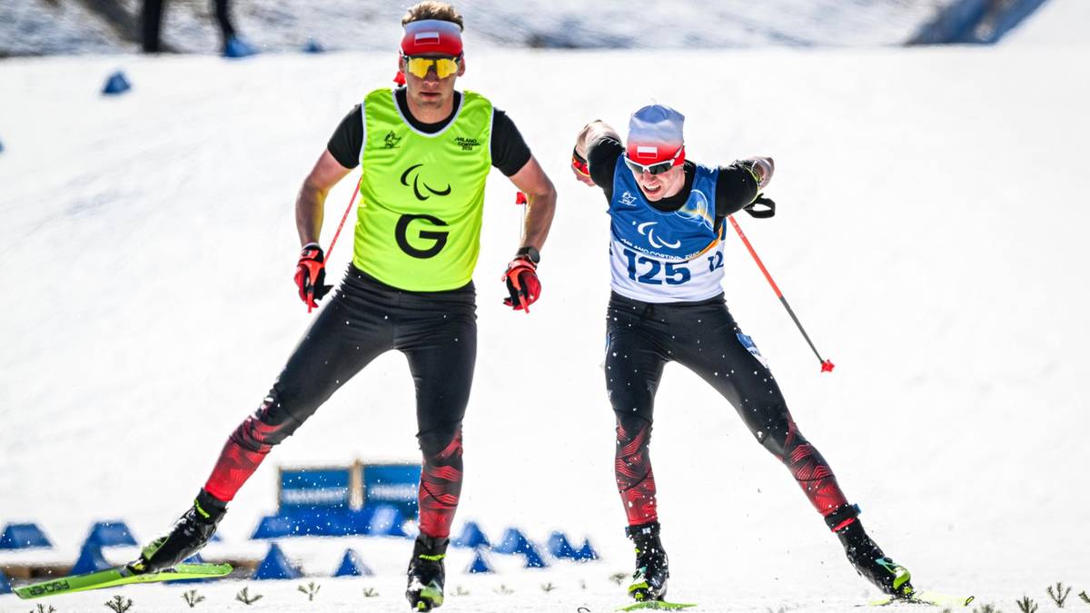 Dw&oacute;ch zawodnik&oacute;w narciarstwa biegowego w strojach sportowych z numerami startowymi i oznaczeniami paraolimpijskimi na śnieżnej trasie.