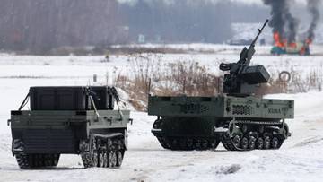 Dwa pojazdy wojskowe na zaśnieżonym polu, w tle płonący budynek z dymem.