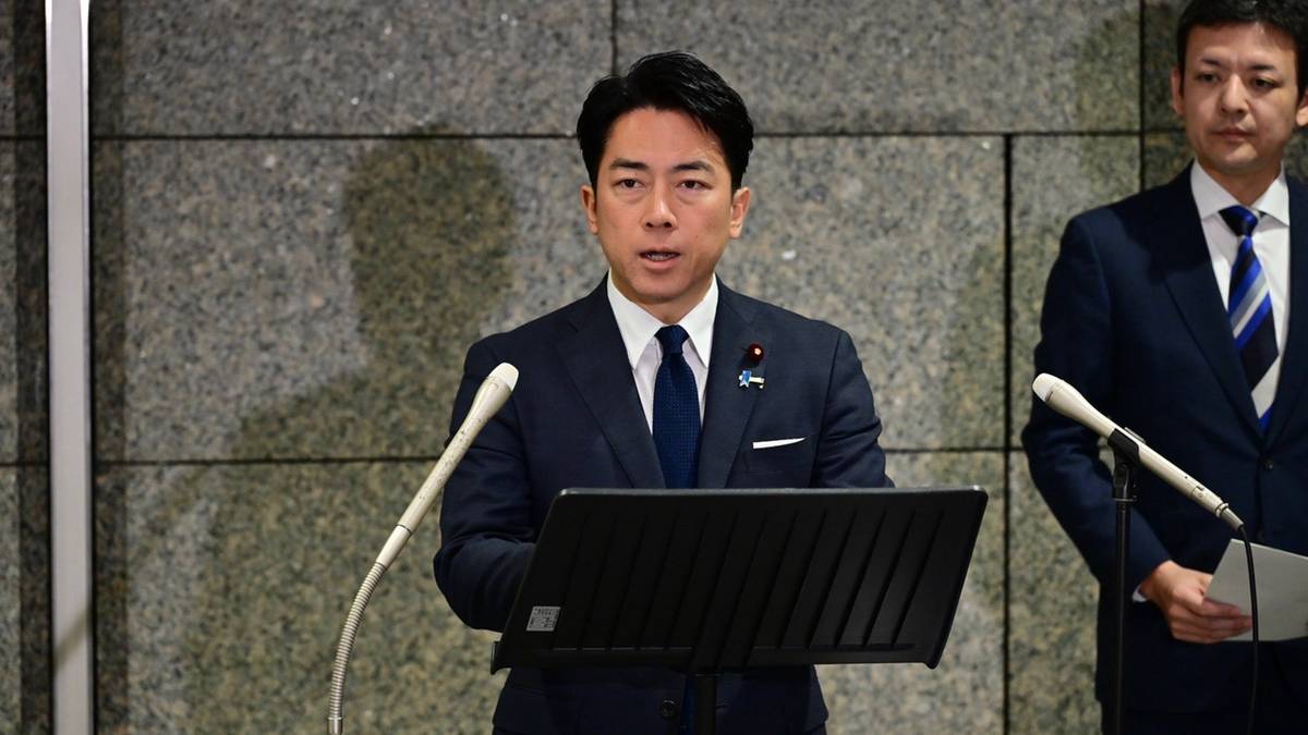 Mężczyzna w garniturze przemawia do mikrofonu, za nim stoi drugi mężczyzna.