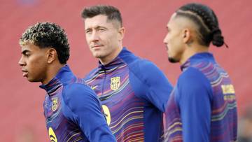 Trzech piłkarzy FC Barcelony w niebieskich strojach treningowych, z Robertem Lewandowskim w środku.