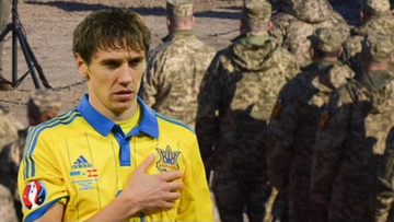 Piłkarz w koszulce reprezentacji Ukrainy z ręką na sercu na tle żołnierzy w mundurach.