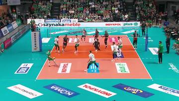 Boisko do siatk&oacute;wki z zawodnikami w akcji podczas meczu, w tle trybuny z kibicami.