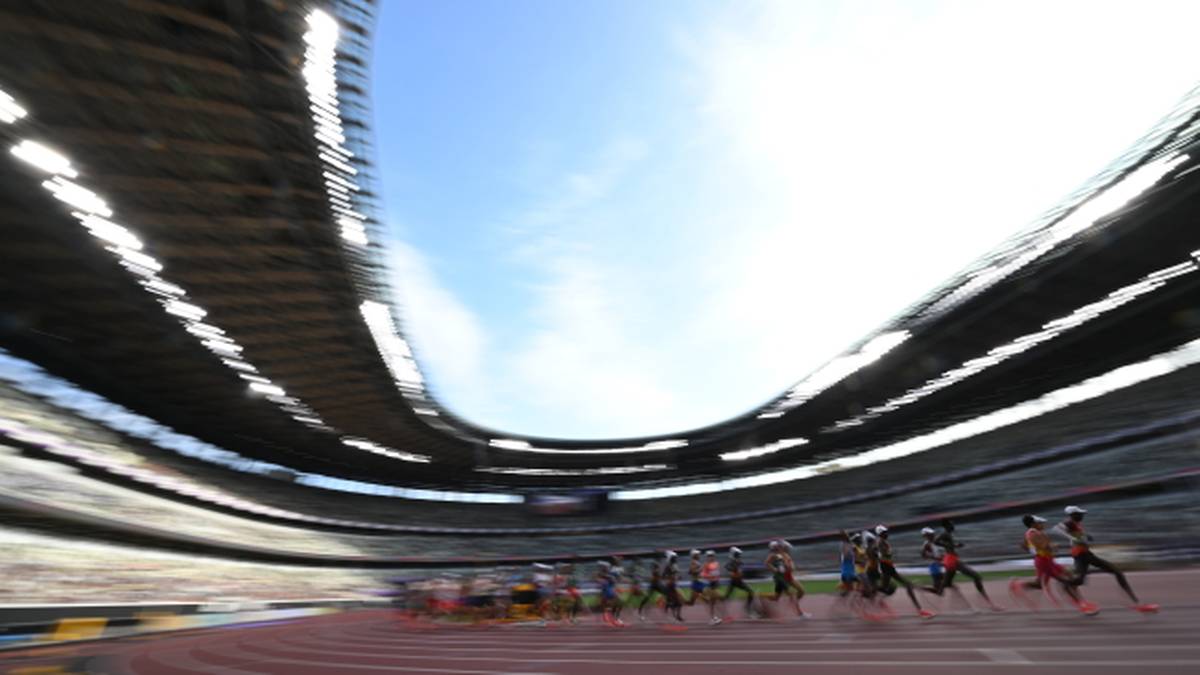 Grupa lekkoatletów biegnąca na bieżni stadionu podczas zawodów. Widoczny fragment stadionu z trybunami.