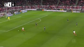 Widok z g&oacute;ry na mecz piłki nożnej pomiędzy RB Lipsk a Eintrachtem Frankfurt. Wynik na tablicy to 1:0 dla RB Lipsk. Gracze w białych i czarnych strojach poruszają się po zielonej murawie.