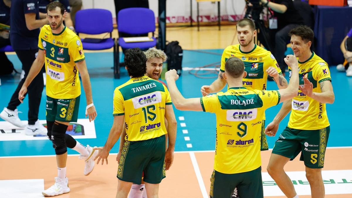 Grupa siatkarzy Aluron CMC Zawiercie w żółto-zielonych strojach świętuje na boisku, okazując sobie radość i wsparcie.