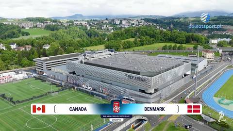 Hala widowiskowo-sportowa "BOK ARENA" z boiskami treningowymi w tle. Na dole obrazu wyświetlany jest baner z flagami Kanady i Danii, wskazujący na mecz pomiędzy tymi reprezentacjami.