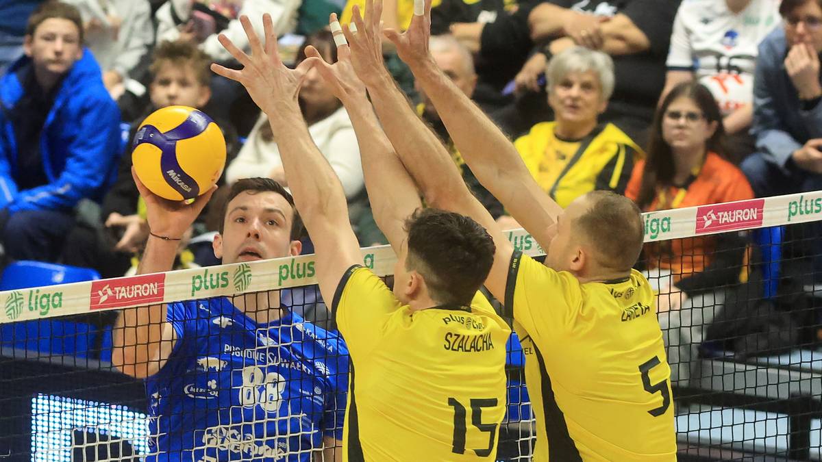 Siatkarz w niebieskiej koszulce z numerem 88 wykonuje atak, blokowany przez trzech zawodników w żółtych koszulkach.