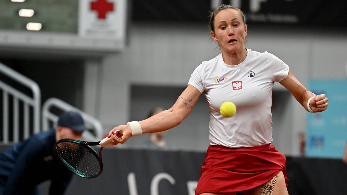 Tenisistka Katarzyna Kawa w białej koszulce i czerwonej sp&oacute;dniczce, z rakietą tenisową, uderza piłkę.