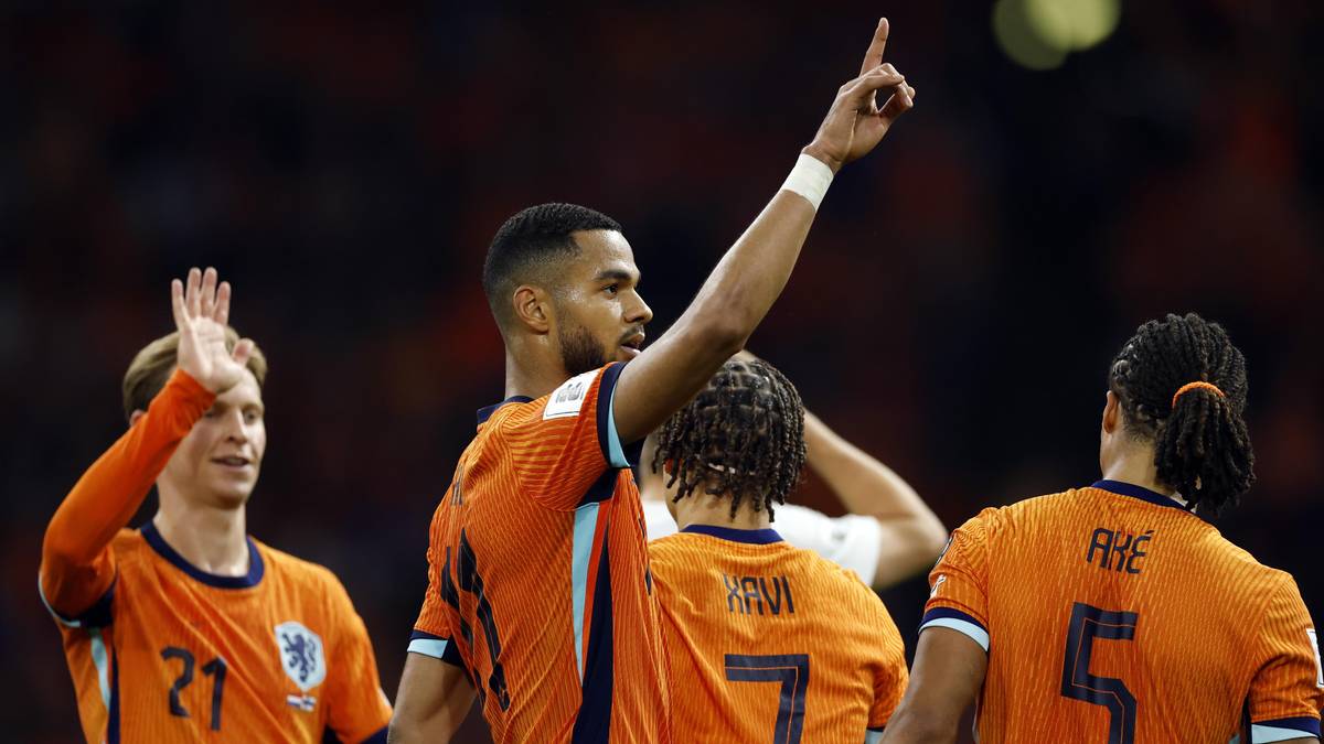 Piłkarz w pomarańczowej koszulce podnosi palec wskazujący do góry, podczas gdy jego koledzy z drużyny go dopingują.