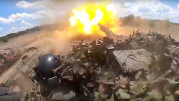 Wybuch w terenie pag&oacute;rkowatym z widocznym na pierwszym planie fragmentem sprzętu wojskowego.