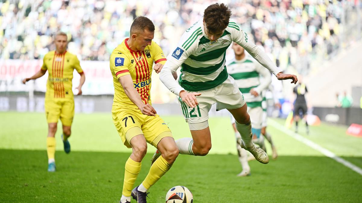 Dwóch piłkarzy rywalizuje o piłkę na zielonej murawie stadionu.
