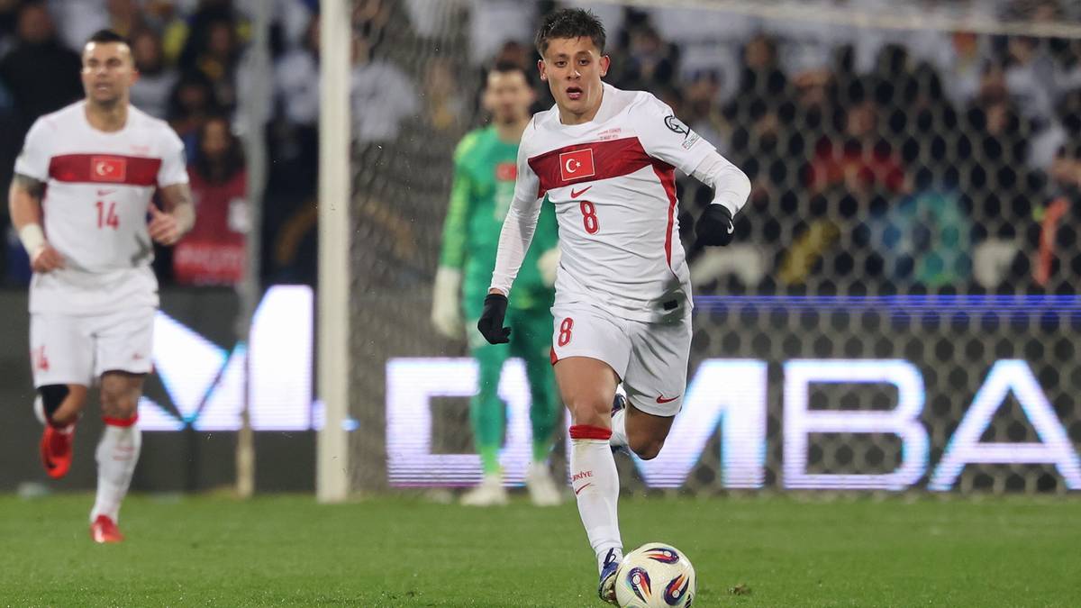 Piłkarz w białej koszulce z numerem 8 prowadzi piłkę na boisku piłkarskim.